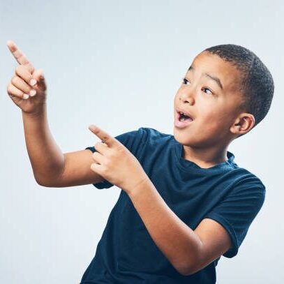 Studio shot of a cute little boy pointing and looking amazed against a grey background