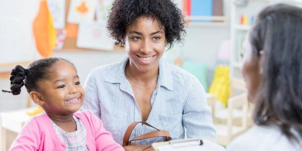 Young African American mom has a conference with her young daughter's preschool teacher. The little girl is sitting next to her mother.